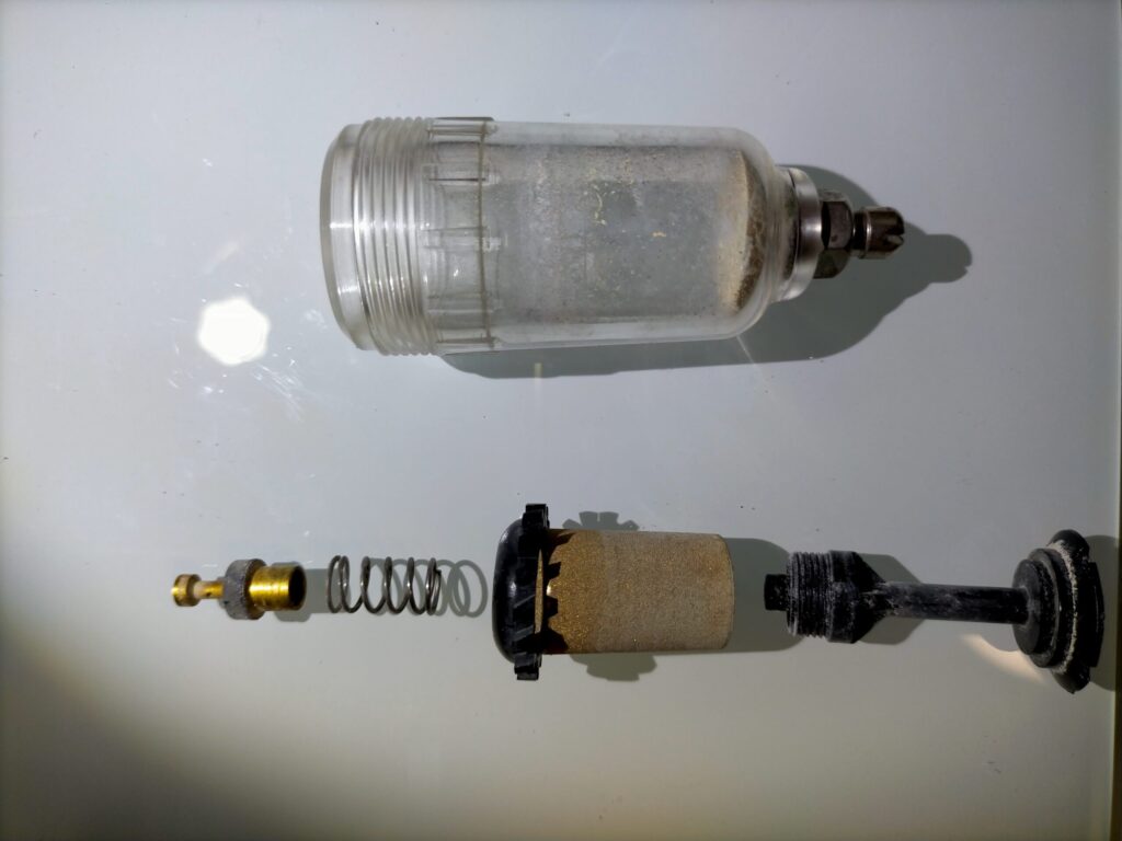 アネスト岩田 IS-925 エアレギュレーター分解後の全部品。ガラスケース・モイスチャーフィルター・真鍮製ジェット（細管内に白い粉が詰まっていた）・各パーツを並べた状態。水洗いとエアガンによる清掃前