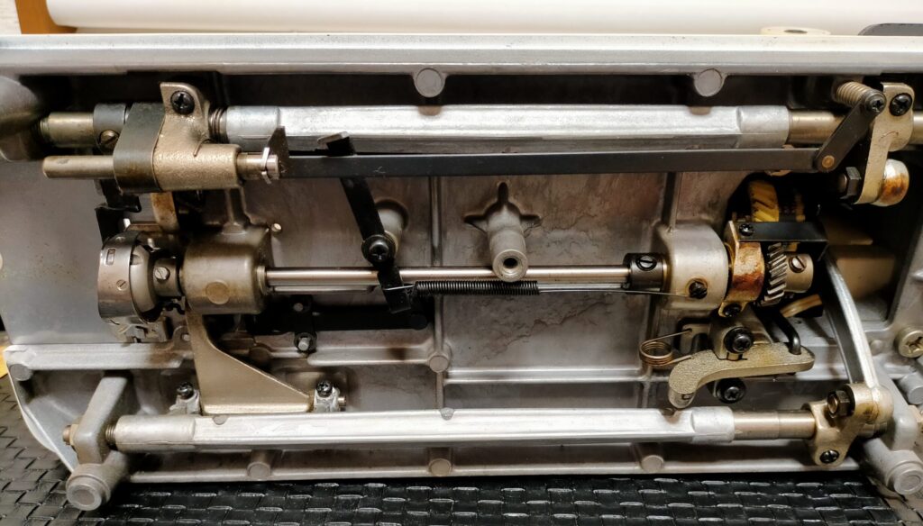 brother TA3-B627 職業用ミシンの底カバーを5本の止めネジを外して取り除いた後の内部実写。釜(水平全回転釜)・駆動ギア・各可動部が露出した状態。釜固定ネジ3本の位置と釜本体が確認できる。各部清掃・注油・釜調整前の内部状態