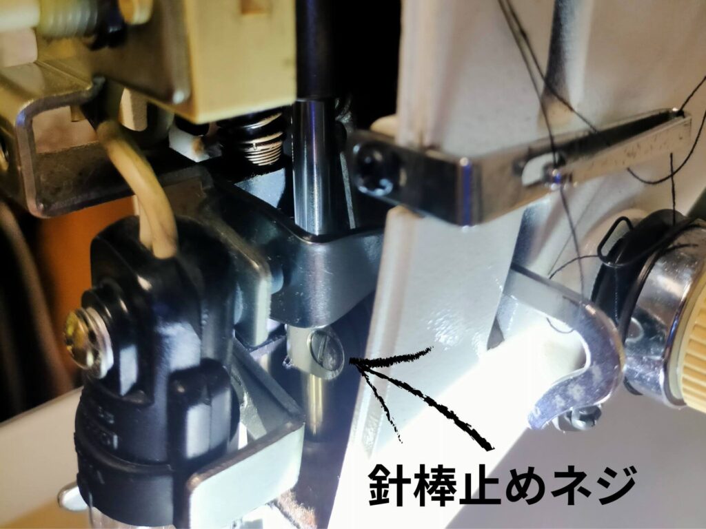 brother TA3-B627 職業用ミシンの針棒調整手順②。側面カバーを外した後の針棒止めネジの位置を示した図解。針棒止めネジを緩めて針棒を上下させ、針棒最下線がツラ位置になるように調整する。釜調整前の必須準備作業
