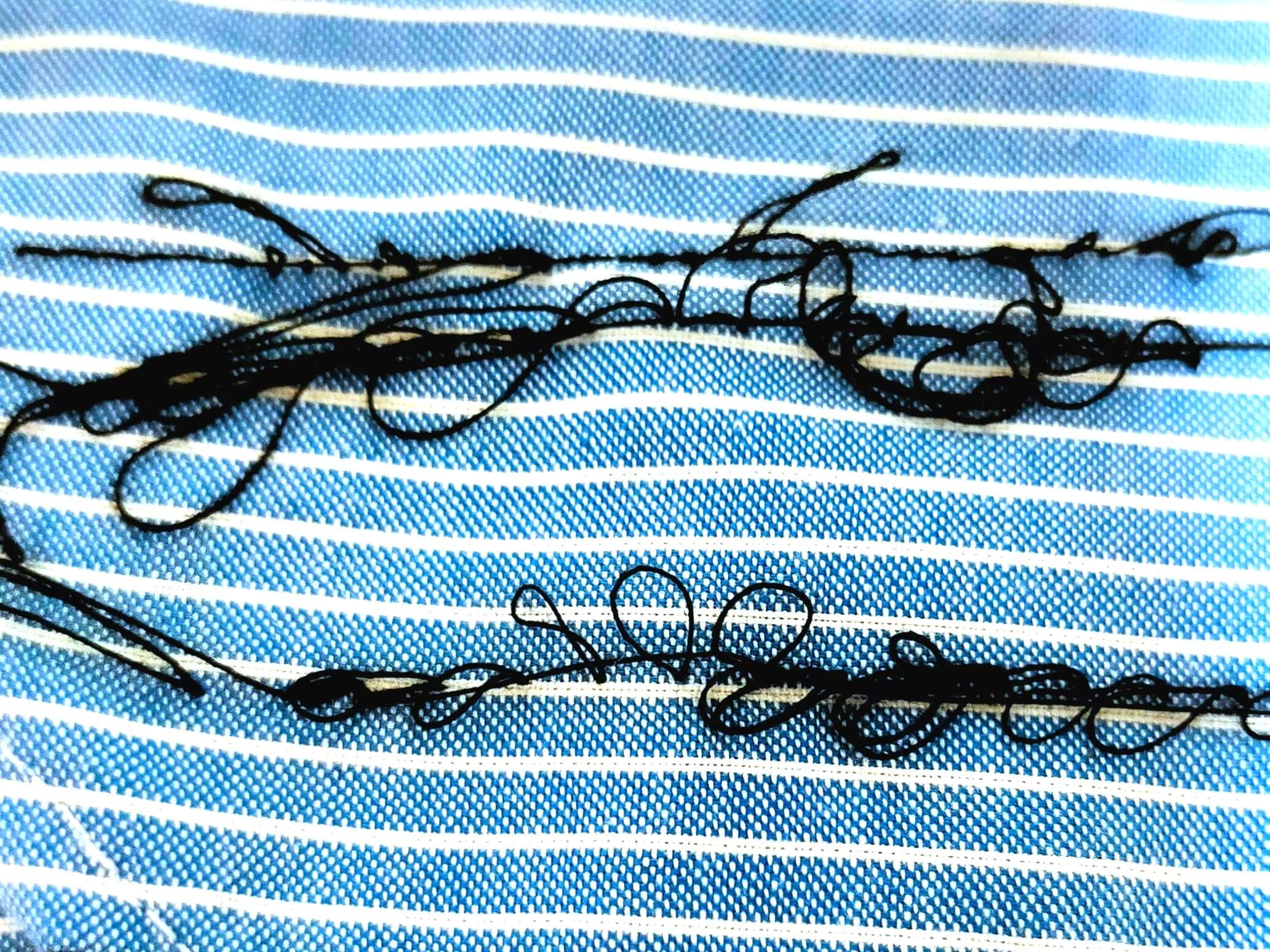 brother TA3-B627(Nouvelle Couture SPECIAL Ⅱ)職業用ミシンで下糸がぐちゃぐちゃになった縫い目の状態。糸調子ツマミの締め込みが甘いことが原因で、下糸がたるんで布の裏面に大量の糸がループ状に出ている。ボビンケース調整ではなく上糸の糸調子を強く締めることで改善する