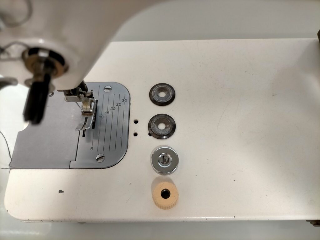 brother TA3-B627 職業用ミシンの糸調子ネジを外し、ツマミから糸調子皿まで全パーツを順番に並べた分解写真。糸取りバネ(ピンピン)・糸調子皿・スプリングの各部品を確認。糸と接触する糸調子皿は真鍮ワイヤーブラシで磨いて清掃