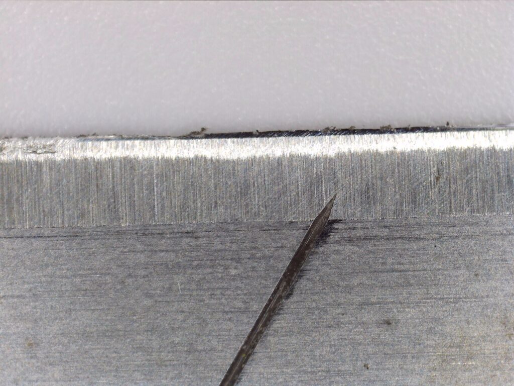 Koolertron デジタル顕微鏡によるカッターの刃の高倍率観察画像②。刃こぼれの細部と粘着物の付着状態が鮮明に写っている。低倍率との比較で分かるデジタル顕微鏡の高倍率観察能力。300倍・5メガピクセルで撮影