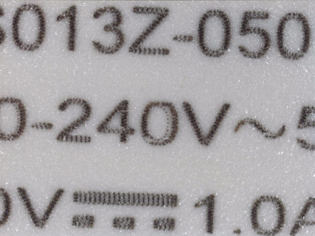 Koolertron デジタル顕微鏡でスマートフォン充電器に印刷された文字「240V」を高倍率観察した画像。「0」の字にドット印字の二重のカスレまで鮮明に確認できる。虫眼鏡（2倍）・ルーペ（30倍）では確認不可能だった細部がデジタル顕微鏡では鮮明に見える比較実例