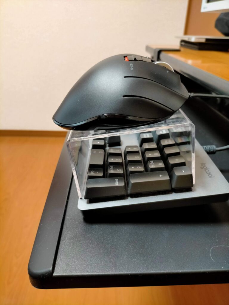ロジクール K840 フルキーボード（テンキー付き）上にセリア「ディスプレイスタンドS」（高さ6cm・内寸92mm）を跨がせ、エレコム トラックボールマウス（M-XT2URBK）を乗せた状態。キーボードスライダー（サンワ 100-KB004）でマウス置きスペースがない問題の100均解決策。テンキー部分の幅に神フィット