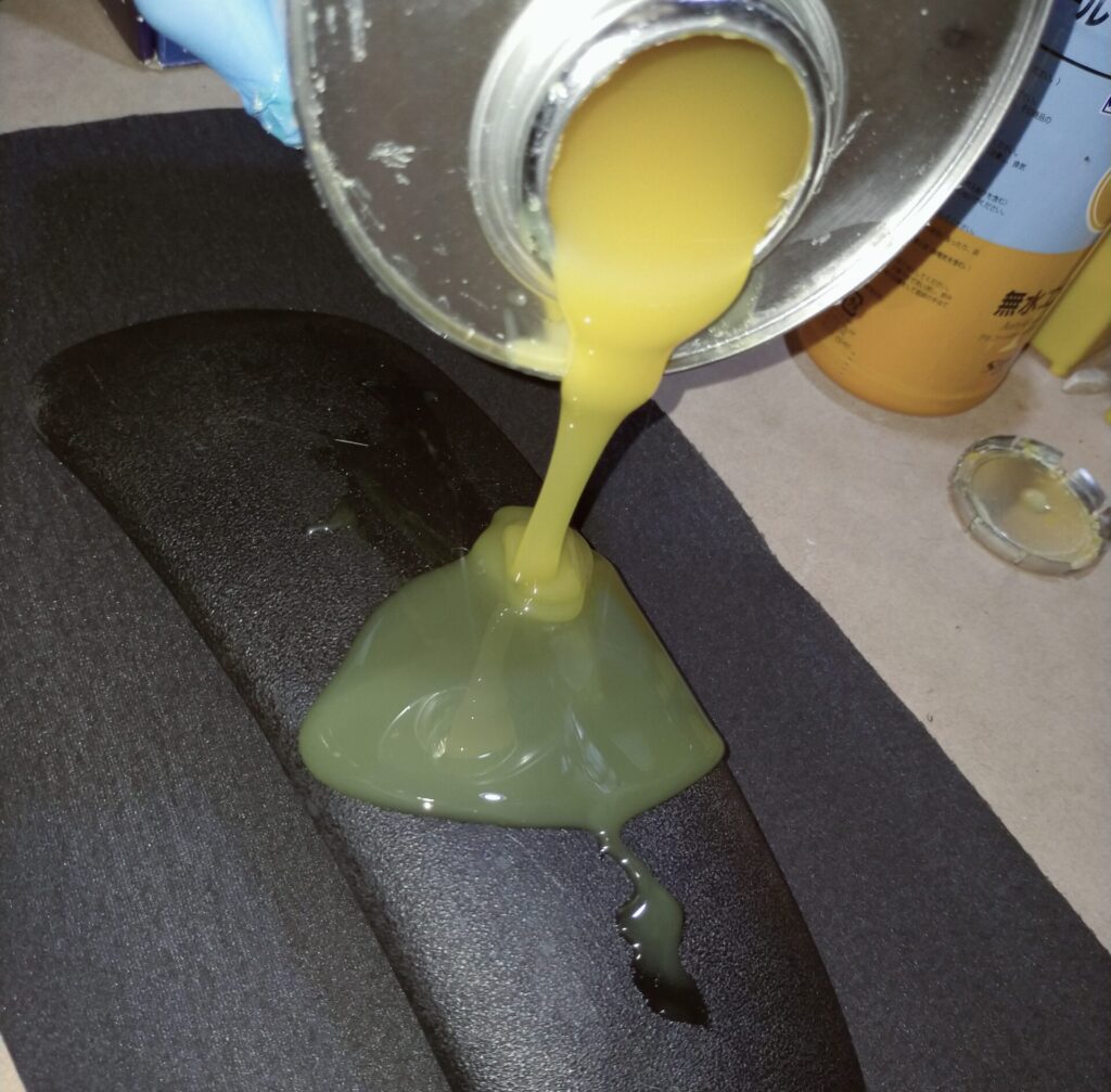 オカムラ コンテッサ肘パッド修理STEP4・肘パッド本体と合皮はぎれの裏面（両面）にコニシボンドG10Zをヘラで薄く均一に塗布している作業。ムラなく均一に伸ばすほど仕上がりが美しく剥がれにくくなる