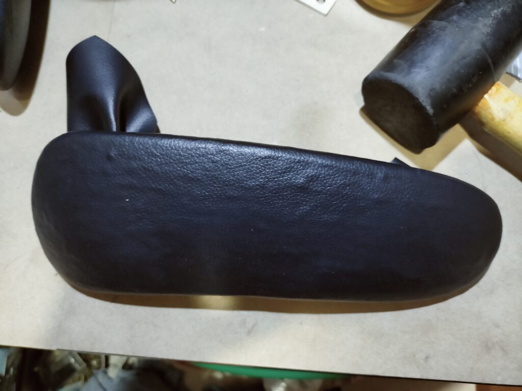 オカムラ コンテッサ肘パッド修理STEP6・オープンタイム完了後に合皮はぎれをシワが入らないよう引っ張りながら肘パッドに貼り合わせている作業。貼り合わせ後はゴムハンマーで叩くかローラーで強く圧着する