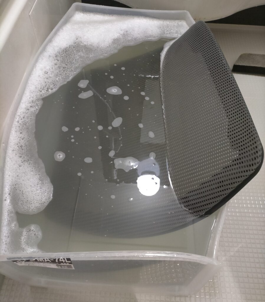 オカムラ コンテッサの背メッシュフレームをバスタブの代わりに衣装ケース（引き出し）に洗濯洗剤とセスキ炭酸ソーダ（消臭効果）を溶かしたお湯で浸け置き後にブラシで擦り洗いしている作業。洗浄工程