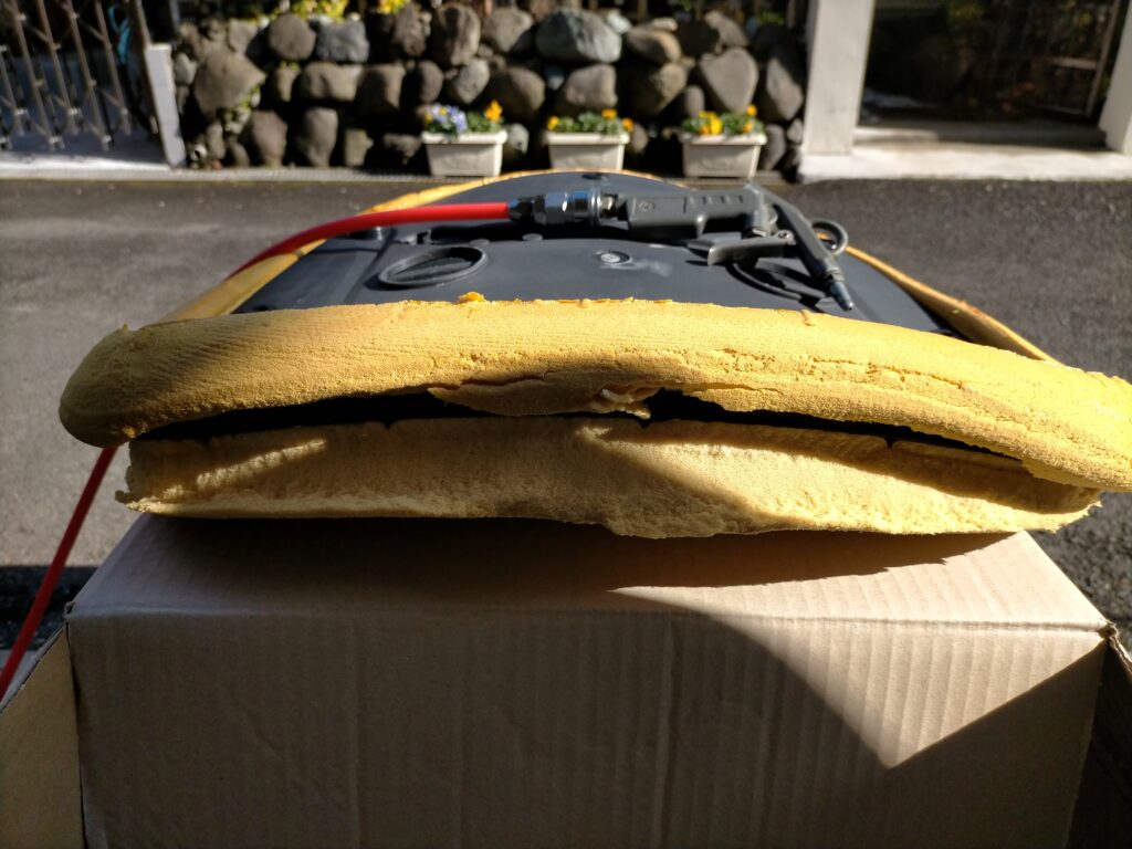 オカムラ コンテッサの座面から取り出したウレタンクッションをエアダスターで粉を吹き飛ばした後にセスキ炭酸ソーダ水を吹きかけ乾いた布で叩き洗いして汚れ・臭いを除去している作業。アルコール消毒と天日干しで完全消臭