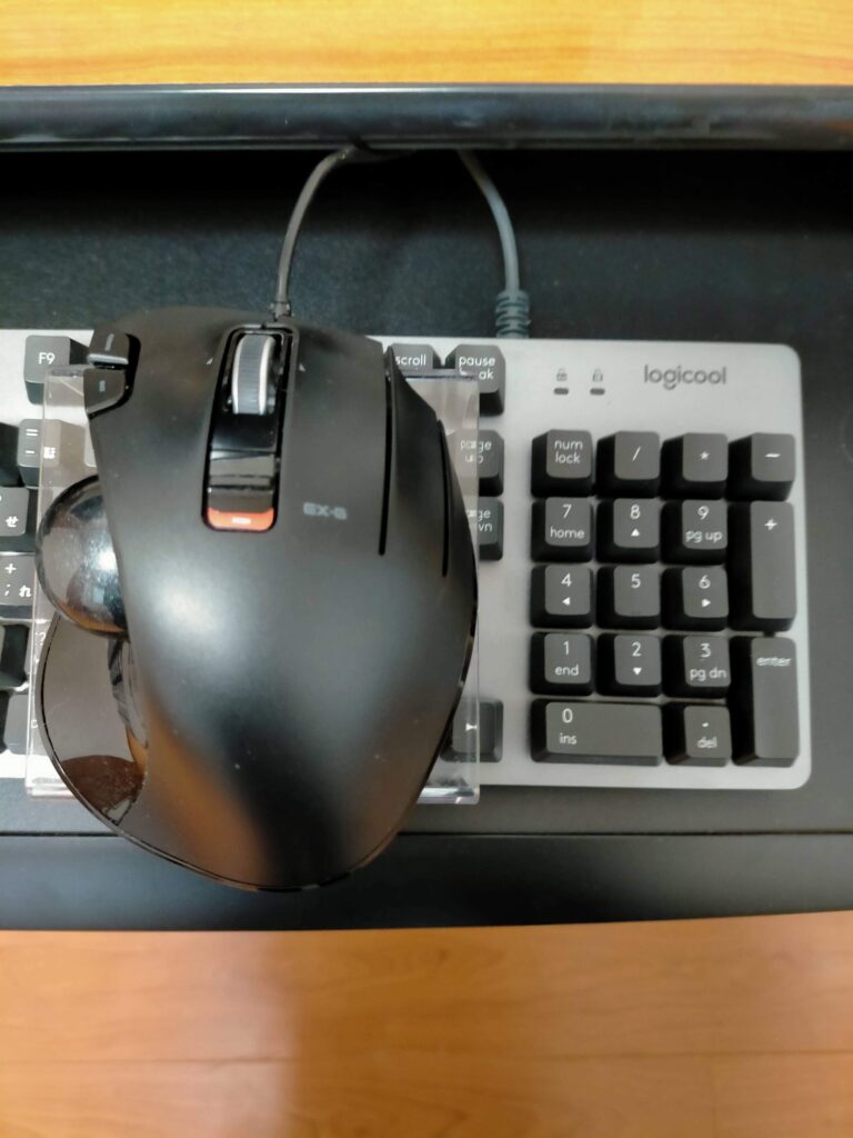 セリア「ディスプレイスタンドS」にエレコム トラックボールマウス（M-XT2URBK）を乗せたままロジクール K840 キーボード上を左右にスライド移動できる状態。内寸92mmがテンキー幅にフィットして脱落しない。キーボード上の好きな位置（テンキー上など）にマウスを自由に配置可能