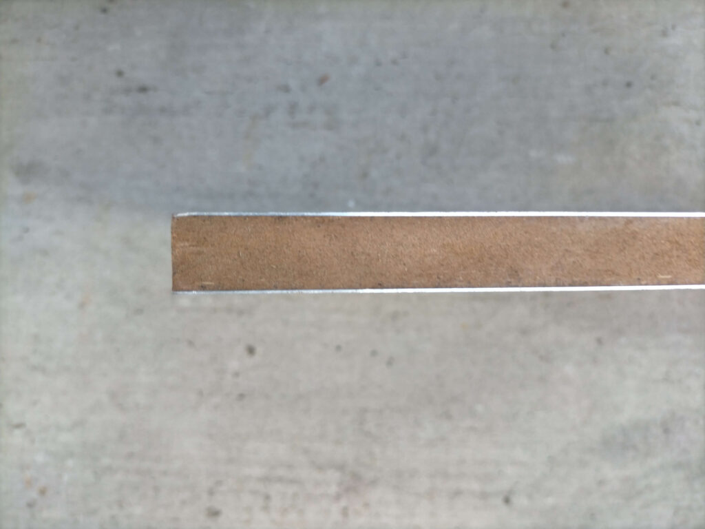 GSメタルシートMS-2の上に敷く15mm MDFボードに0.5mm厚アルミ板を両面接着した床材の縦方向断面・側面写真。厚さ15mmのMDFボードとアルミ板の積層構造を確認できる。体重がかかるとMS-2の気泡が潰れて断熱性能が落ちる問題への対策として検討したスタイロフォーム代替の参考データ