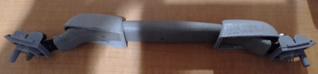 いすゞコモ（E25キャラバン）助手席上のアシストグリップ裏カバーをウェザーストリップの隙間から引き出している作業写真。クリップを破損しないよう後ろ端から真っ直ぐ引き抜く取り外し作業実施例。内張り剥がしKTCハンディリムーバーATP2014を使用