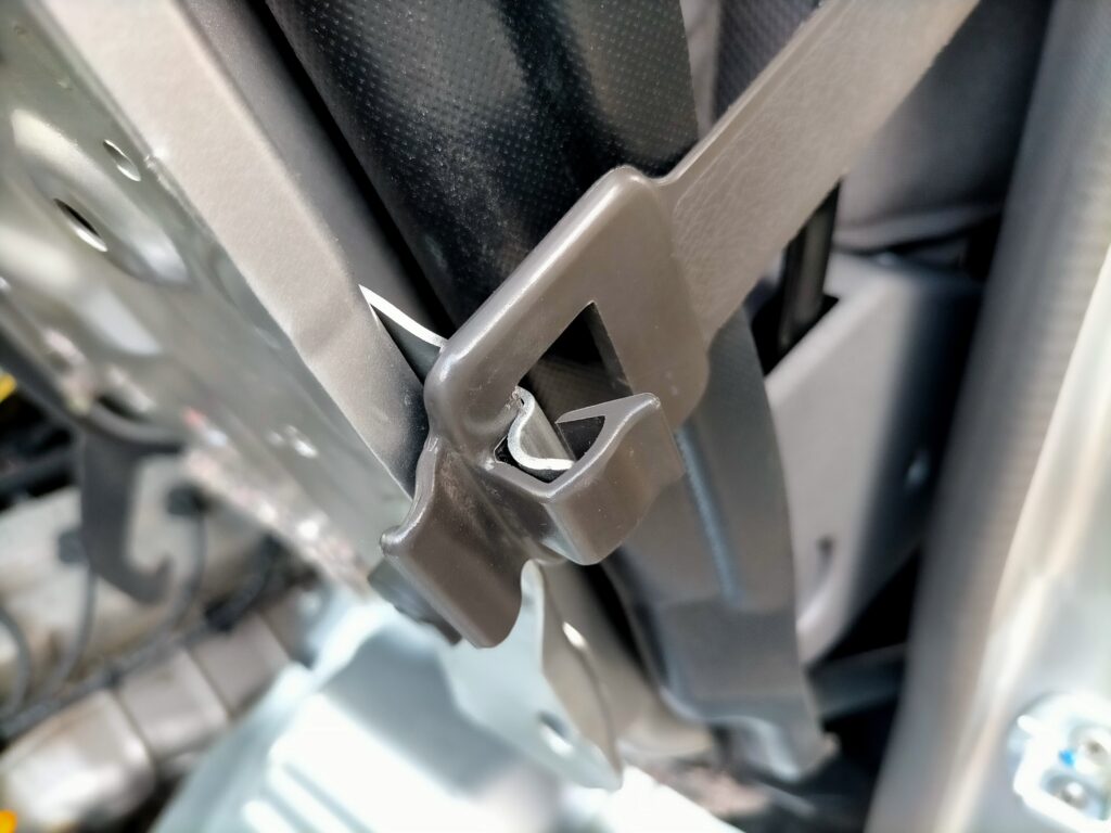 E25キャラバン／コモのエンジンアクセス手順ステップ4・跳ね上げた助手席シートを左センターピラー（助手席シートベルト付近）のフック付きベルト（吊り具）に固定した状態。吊り具で固定することで作業中にシートが落下するリスクを排除。この状態でKA24DEエンジンの上抜きオイル交換作業が安全に行える