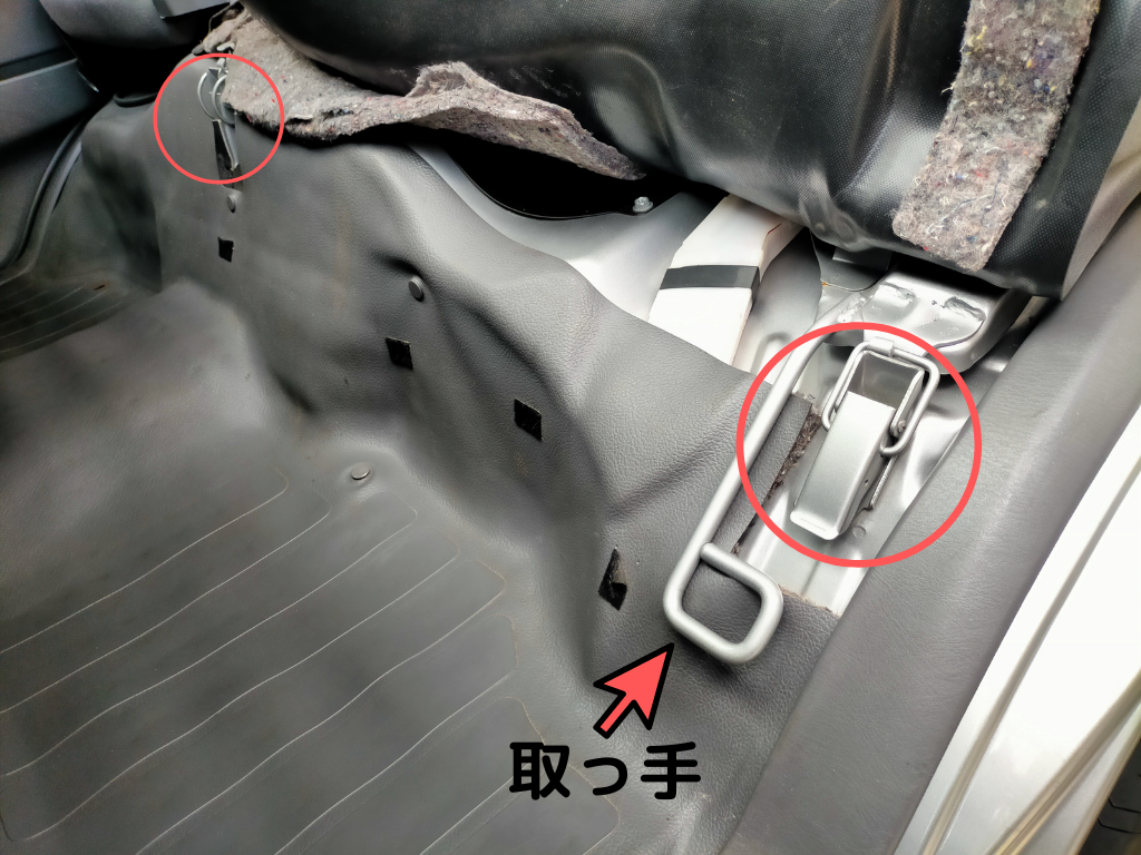 E25キャラバン／コモのエンジンアクセス手順ステップ1・助手席後ろのカーペットをめくって現れるエンジンカバーの2箇所ロック取っ手の位置図解。このロックを外してから助手席の背もたれを前に倒し座席ごと持ち上げることでKA24DEエンジンルームにアクセスできる