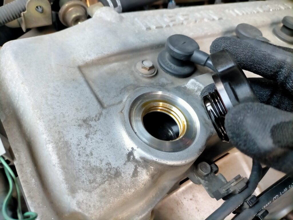 E25キャラバン／コモ（KA24DE）上抜きオイル交換ステップ4・エンジン上部のオイルフィラーキャップを開けた状態。新しいオイルはこのキャップ口からオイルジョッキで注入する。日産純正SNスペシャル5W-30を規定量注入。20Lペール缶なら約5回分使用可能でコスパ最強