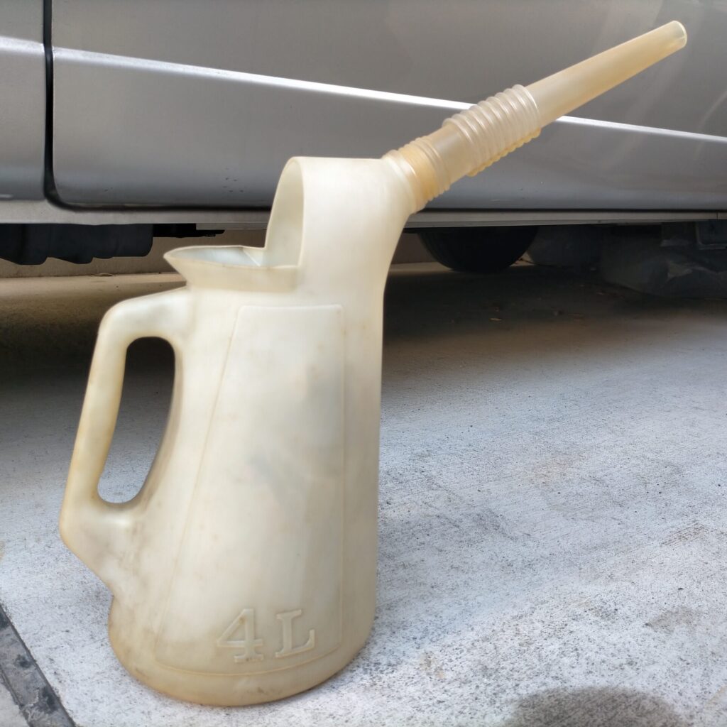 E25キャラバン／コモ（KA24DE）上抜きオイル交換ステップ4・古河薬品工業KYK ロングノズルオイルジョッキ（90015）で日産純正SNスペシャル5W-30を注入している工程。ロングノズルタイプのジョッキはキャブオーバー車のような深い位置のフィラーキャップへの注入に便利。規定量を正確に入れることが重要