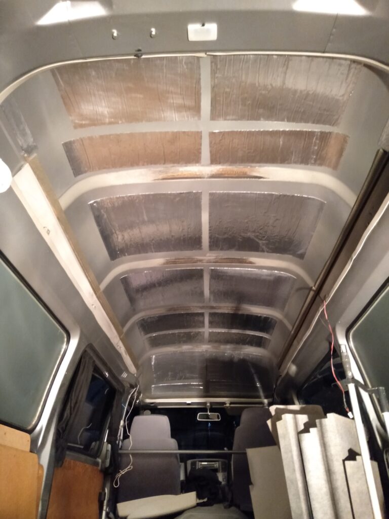 日東電工レジェトレックスD-300N（1.5mm×500mm×1000mm）を短冊状にカットしてシリコンオフ脱脂済みのいすゞコモ（E25キャラバン）天井鉄板に貼り付けた施工状態。響きやすい箇所を中心に全体の3〜5割程度貼りルーフバー通過箇所を避けた配置。コロコロ代用の失敗を防ぐ専用圧着ローラー（TRUSCO POMR-SS）での圧着前の状態