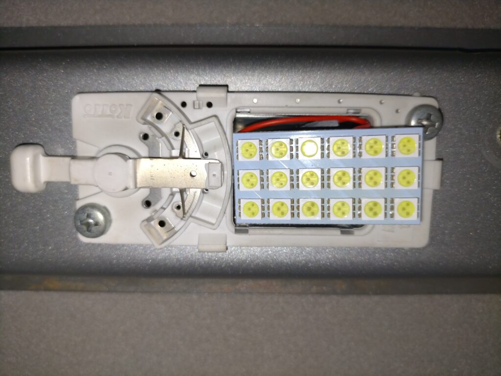 いすゞコモ（E25キャラバン）のルームランプ（2箇所）をプラスネジで取り外した状態。バッテリーマイナス端子切り離し後にアシストグリップと合わせて取り外す。ショート防止処置後の配線切り離し作業