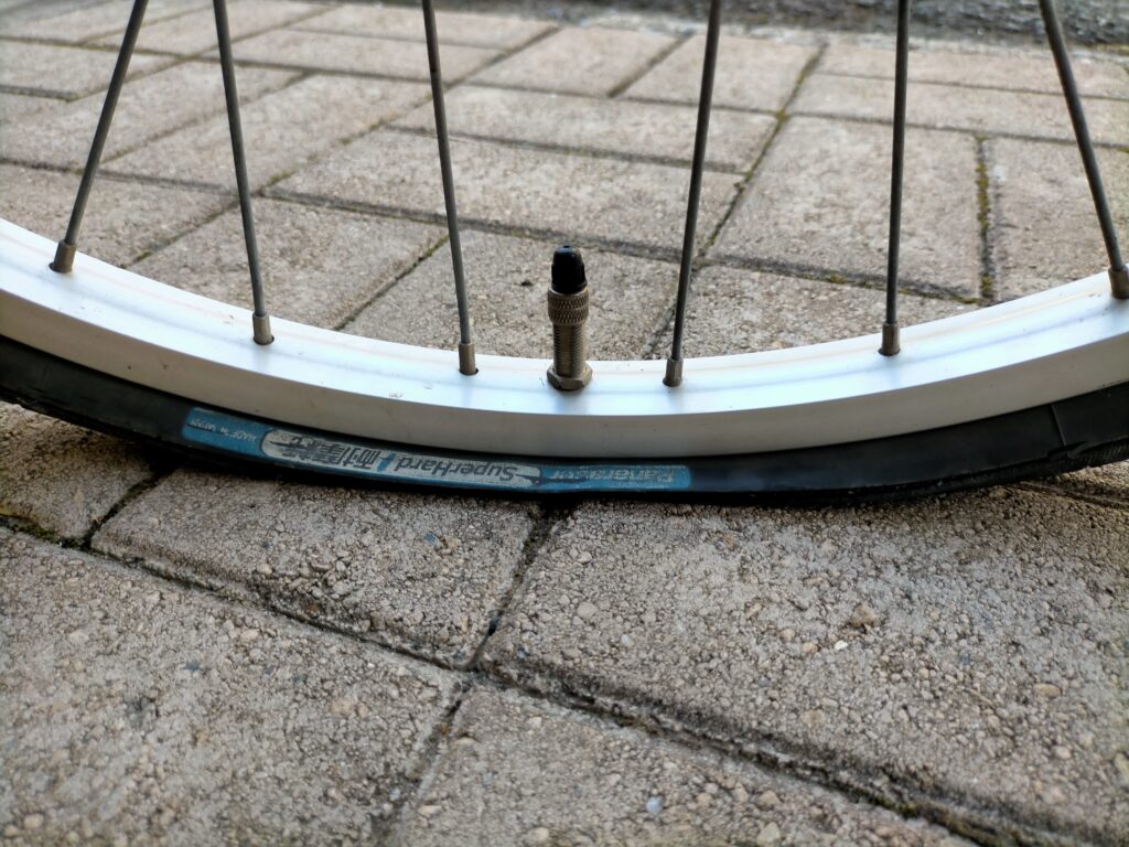自転車パンク修理ステップ1・虫ゴム交換の最初の手順。英式バルブ先端のゴムキャップ（バルブキャップ）を指で取り外している状態。ゴムキャップはほぼすべての英式バルブ自転車（ママチャリ・電動自転車）に共通の部品