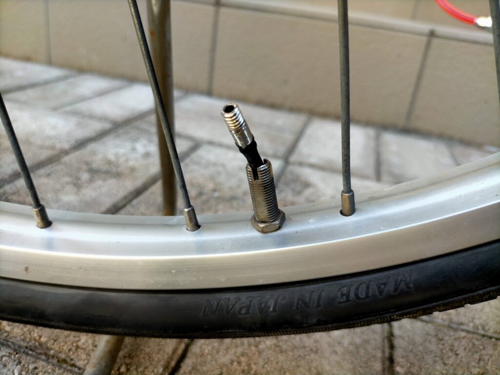 自転車パンク修理ステップ1・虫ゴム交換の手順3。英式バルブからプランジャー（弁棒・中心の棒状部品）を指で引き抜いている状態。プランジャー先端に虫ゴムが付いており、この虫ゴムの劣化が空気漏れの最多原因