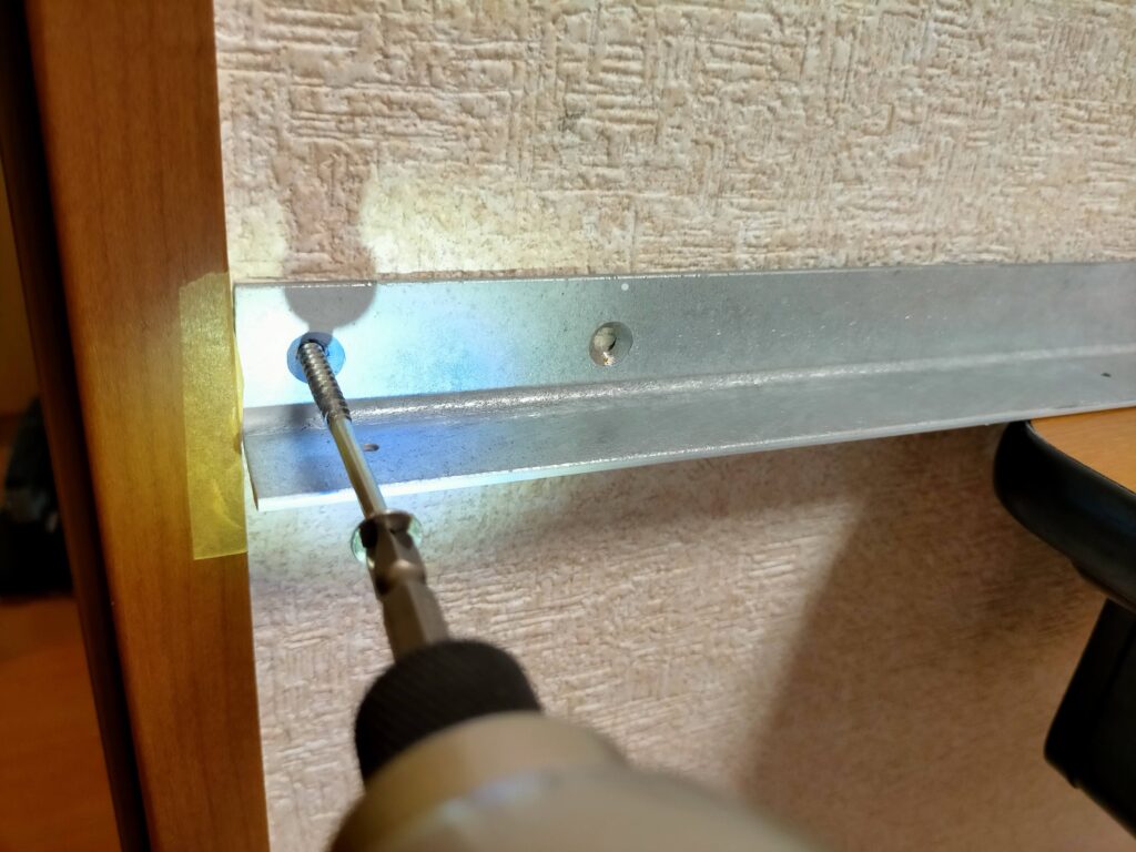 空中デスクDIYアングル取り付け工程・白塗装済みアングルを壁の柱・間柱に4.8×75mmコーススレッドで仮固定（両端のみ先止め）している状態。まず両端を仮止めして水平を確認してから全ビスを本締めする手順が水平精度を保つ鍵。インパクトドライバーで打ち込む