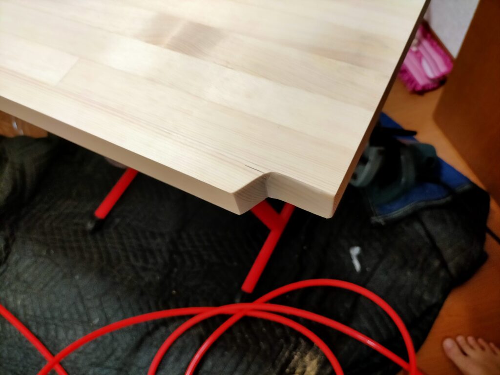 空中デスクDIY・天板を壁にぴったり付けるとコンセント・配線が通せなくなるため、丸ノコと手ノコで天板の一部をカットして配線スペースを確保する加工の準備。コンセント位置を確認しながら天板の切り込み位置を決定している状態。壁付けデスクDIYの必須の配線処理