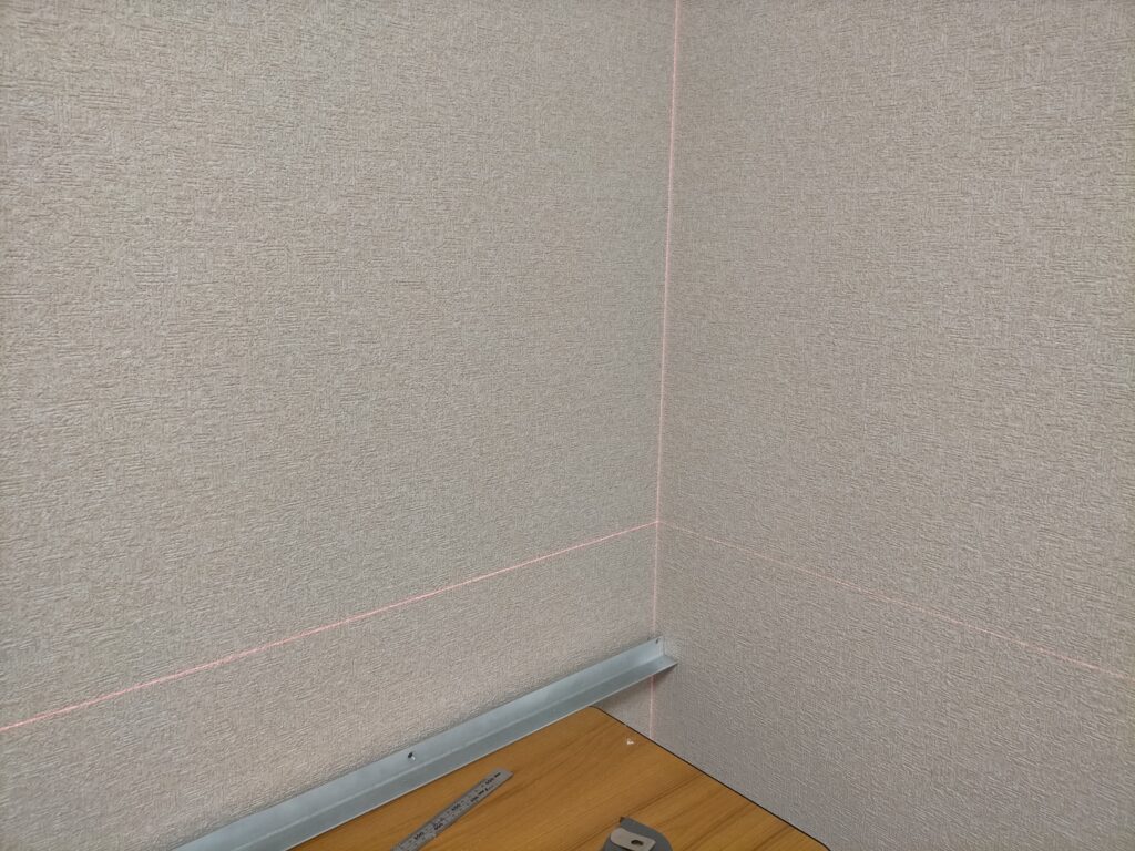 空中デスクDIY墨出し工程・ONE STEP レーザー墨出し器から壁面に照射されたグリーンレーザーラインの状態。壁面にくっきり映るグリーンラインを基準にアングル取り付け高さと水平を決定する。高輝度グリーンレーザーは昼間の室内でも視認しやすい