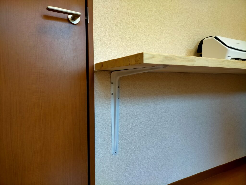 空中デスクDIY・壁がないL字端部分の固定に使用したL型棚受金具（350×400mm・855円）。アングルを使えない壁のない箇所の代替固定具として使用。見栄えはリメイクシートなどで後から整えられるが強度は抜群。L字デスクの壁なし端部の固定問題を解決する実用的なパーツ
