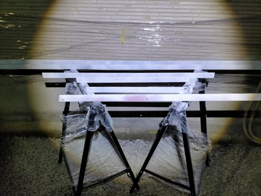 フローティングシェルフ・デスクDIY・アシズケ・サーフェーサー処理後のアングルにパールホワイトのラッカースプレーで仕上げ塗装している工程。1缶で1回塗装分がちょうど使い切りになった。見えない裏面は多少のムラも「味」として許容。白いアングルがパイン材に馴染む仕上がり