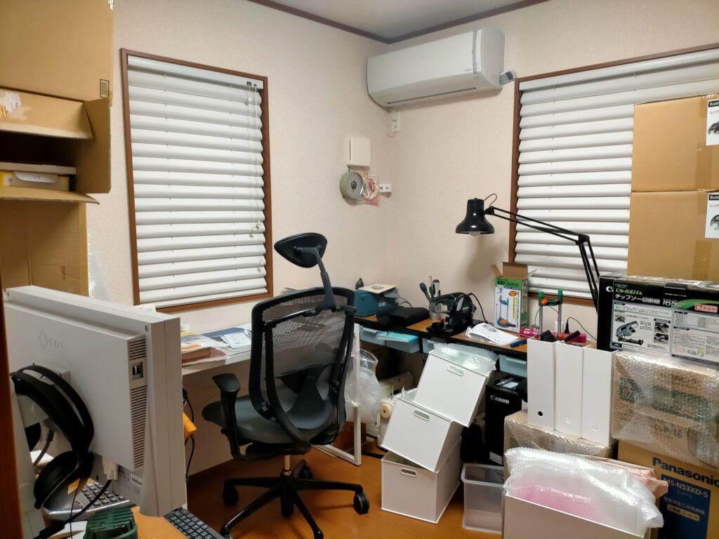 フローティングシェルフDIY施工前・Before写真。物が溢れて足元も窮屈な書斎スペース。既製品の棚では壁サイズに合わず足元に脚があって掃除もしにくい状態。この写真からAfterのフローティングシェルフ設置後の劇的な変化を対比させる