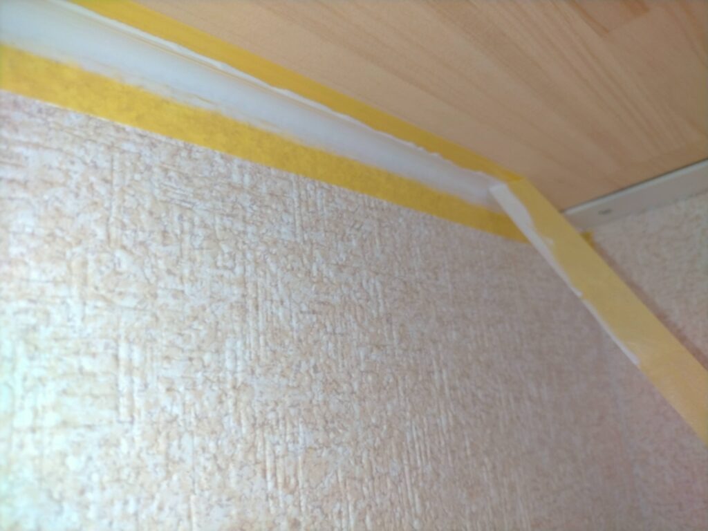 フローティングシェルフDIY・コーキング(ヤヨイ化学ぺネット)が乾く前にマスキングテープを素早く剥がしている工程。コーキング乾燥後に剥がすと塗膜が剥がれるため乾燥前が必須タイミング。マスキングを剥がした後に滑らかでシャープなコーキングラインが現れる