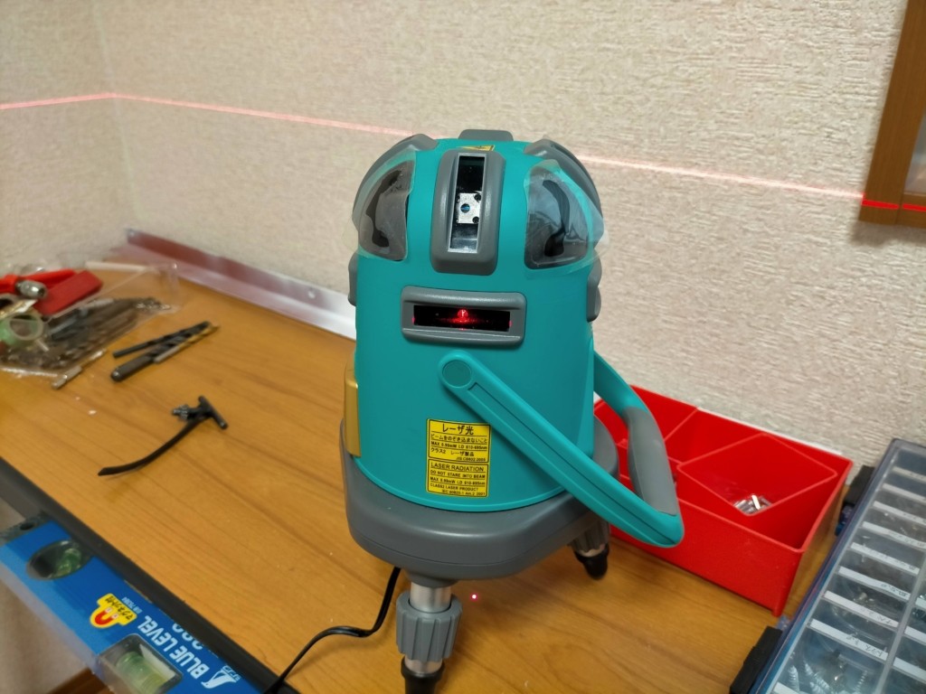 フローティングシェルフDIY・レーザー墨出し器(ONE STEP 5ライングリーン)で壁面の水平ラインを確認している工程。棚の強度と美観は水平精度で決まる。自動補正機能付きで初心者でも正確な水平が取れる。棚アングルの取り付け位置決めの第一工程