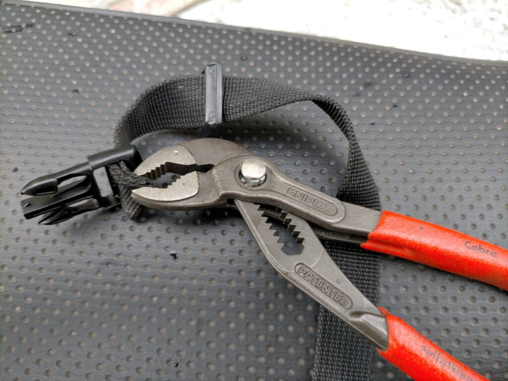 タンクバッグバックル交換STEP2・KNIPEXコブラ 8701-150（150mm）でベルト先端を掴んでNIFCO TSR-20の通し穴に強引に通している工程。シリコンスプレー塗布後にプライヤーで押し込む裏技。3重折り縫製の分厚いベルトも縫製を解かずに通せる