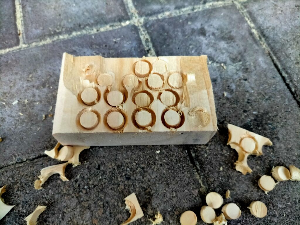 DIYザグリ穴隠し用木ダボの自作工程・端材(同一素材の板)にΦ10木ダボドリル(DBD-10)で適当な長さ分穴をあけている状態。端材は棚・机に使った板の余り材を使うことで木目・色調が完全一致する。100均やホームセンターの10mm丸棒で代用も可(ただし木目・色は合わない