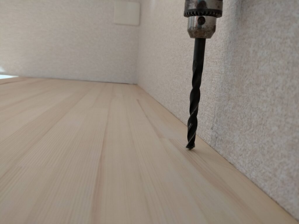 DIYザグリ穴隠しステップ1・10mmキリ(ドリルビット)で板面に垂直に深さ約10mmのザグリ穴をあけている工程。垂直を保つことがビス頭を正確に隠す前提条件。この穴にビス頭が収まることで板面からビスが飛び出さなくなる。5×80mmコーススレッドのビス頭径に合わせた10mm径