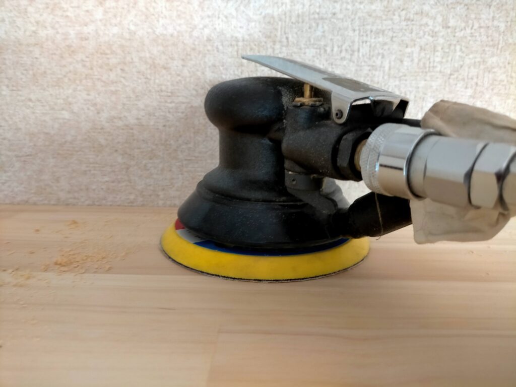 DIYザグリ穴隠しステップ7・木工ボンド硬化後に板面から飛び出した木ダボをのみやサンダーで削り、板面と完全に面一(ツライチ)に仕上げている工程。同一素材の木ダボのため木目・色が板と自然に馴染む。遠目には処置箇所が判別できないレベルの仕上がりになる