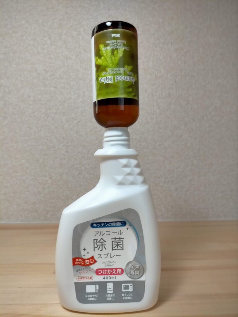 青森ひば油約10mlをアルコール除菌スプレー約100mlに混ぜた抗菌スプレーを調製している工程。ひば油濃度0.01%でカビ・雑菌殺菌効果。MDF材の質量に対して必要量を目安に100均スプレー容器で自作。殺菌後のMDF材全面にスプレーして抗菌コーティング