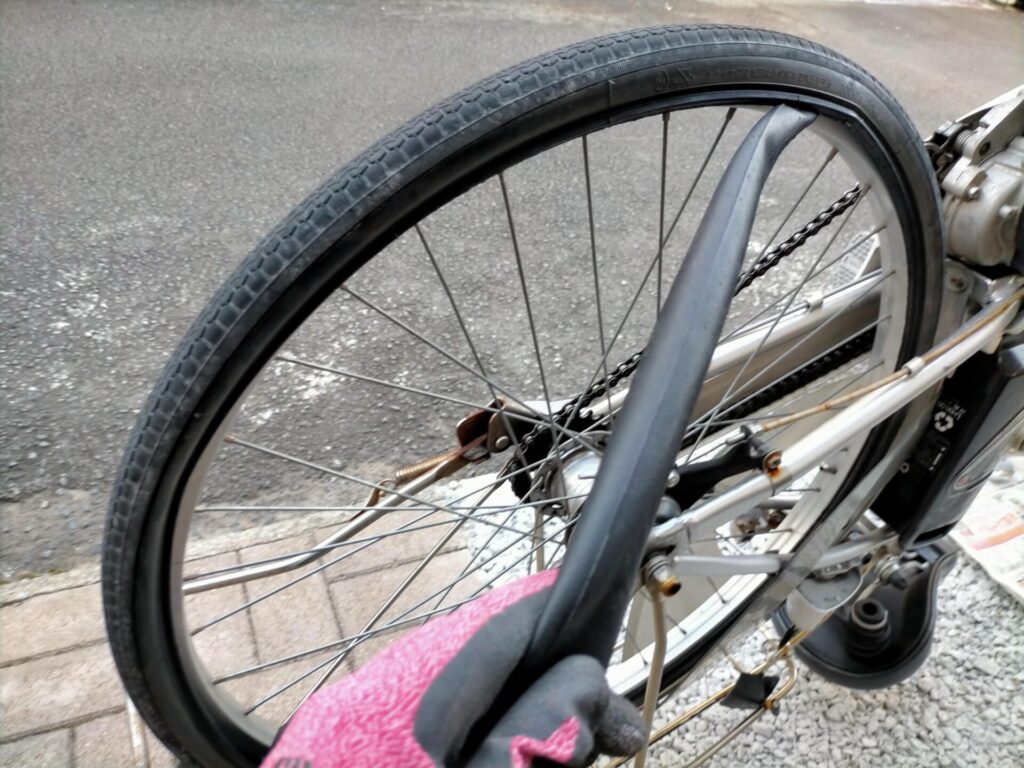 自転車パンク修理ステップ3・タイヤの隙間からチューブ（インナーチューブ）を引き出している状態。チューブ取り出し後にプランジャーとトップナットを一時的に戻して空気を入れ、水入りバケツで気泡確認によるパンク箇所特定を行う
