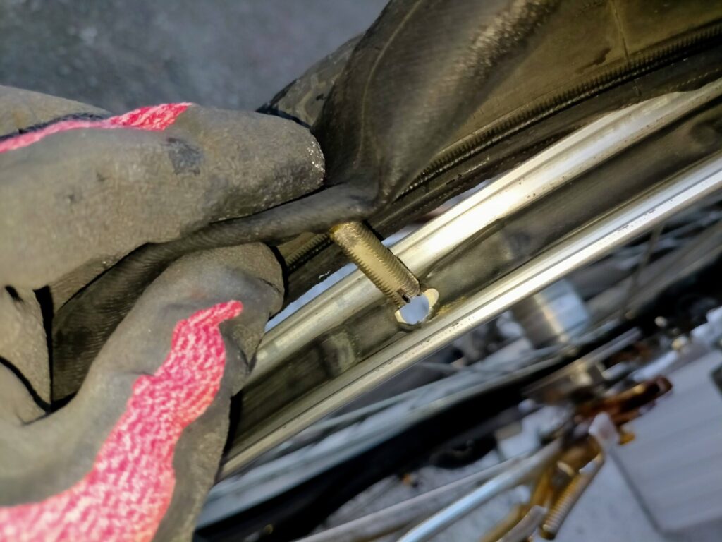 自転車パンク修理ステップ5・修理済みチューブのバルブをリム穴に通して組み戻す工程。バルブ固定ナットを軽く仮止めした後チューブがねじれないようタイヤに収め、なるべく手でタイヤビードをリムにはめ込む（最後だけタイヤレバー使用可）