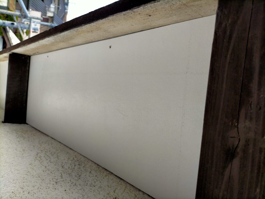 塗装済みケイカル板（6mm）を軒天に3×30mmコーススレッドで仮止めしている高所作業。棟木・母屋の間に正確にはめ込む工程。常に上を向いての作業のため安全を考慮した足場が必須。この後に塗装済み杉角材で本固定する手順