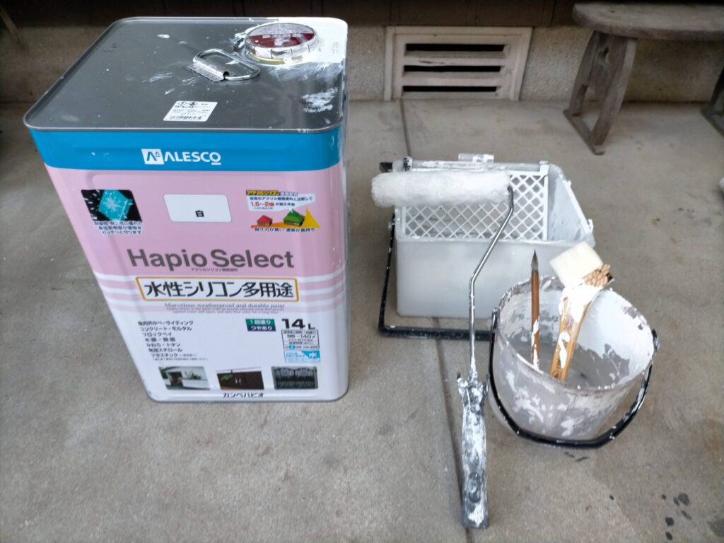 カチオンシーラー下塗り後のケイカル板にカンペハピオ水性シリコン多用途（白）をローラーで上塗りしている工程。取り付け前の地上での塗装によって高所での作業時間を大幅短縮。塗装後に寸法より5mm小さく丸ノコでカット