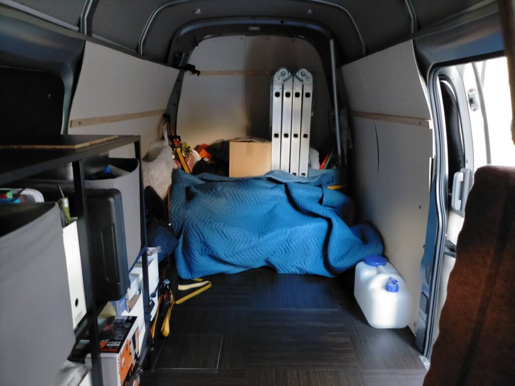 いすゞコモ（E25キャラバン ハイルーフ）荷室に実家DIY修理用の工具・材料と車中泊用寝具を積み込んだ状態。LiTime 12V 2000W純正弦波インバーター（DC12V→AC100V）でスマホ・電動工具バッテリーを走行中充電。布団を敷いても足を伸ばして眠れる広いハイルーフ荷室