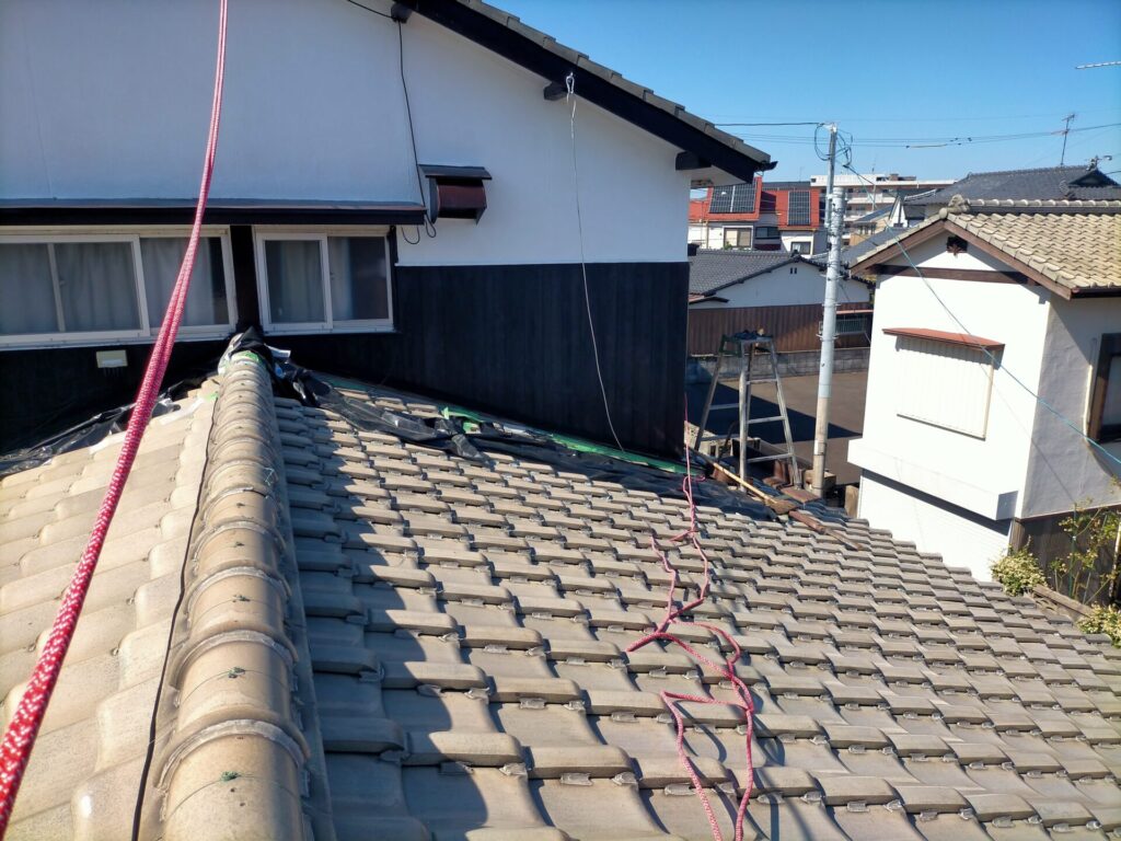 外壁塗装DIYで使用するアルミはしごを瓦屋根に設置した状態。2階外壁作業に使用し右脚にいらかくんHL-36を装着滑り止めに白幡瓦用資材止G-6と角材を使用(引きの写真)