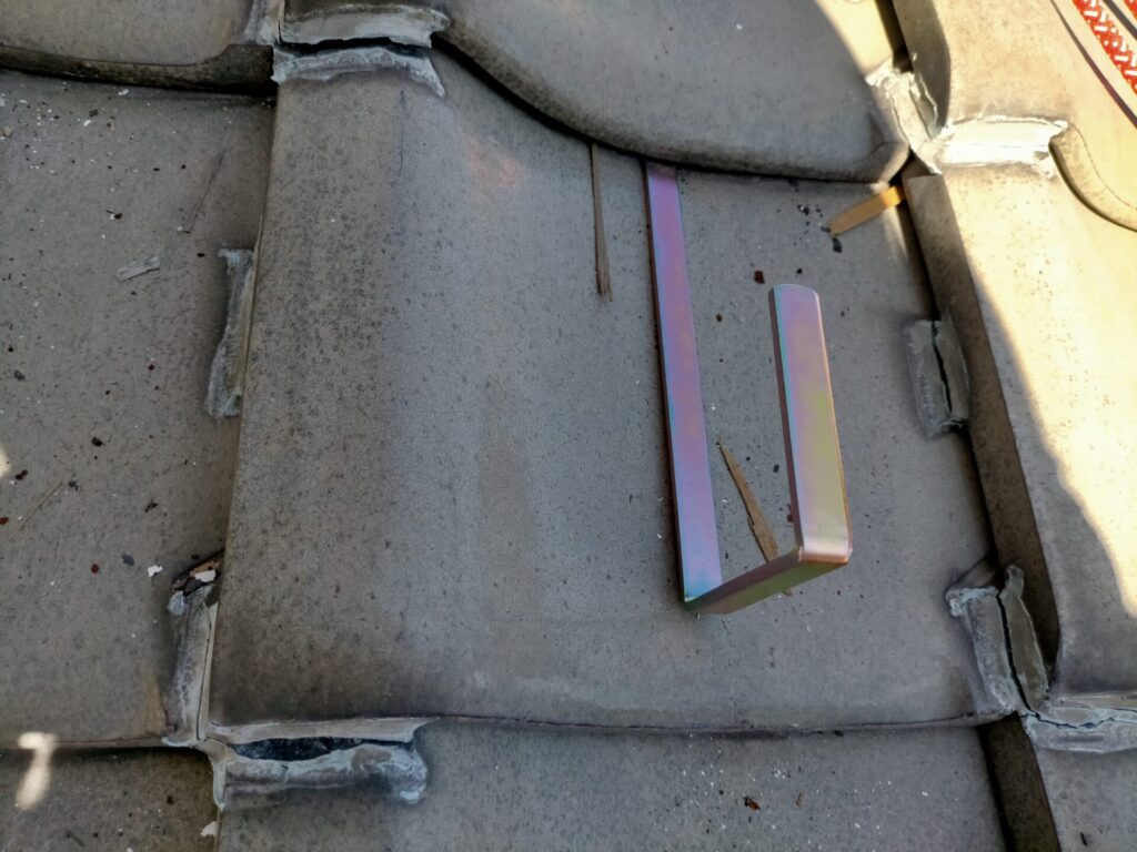 白幡瓦用資材止G-6を瓦に取り付けた完了状態。フックが瓦の下段にしっかり引っかかり資材が乗る水平面が確保された状態。この金具2個に角材を渡してから「いらかくんHL-36」を設置することで屋根上作業面が完成