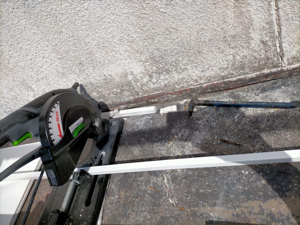 高儀EARTH MANチップソー切断機CS-100TA（165mm）で軒下に持ち込んで塗装済み杉角材（15×15mm）を現場寸法に合わせて切り出している工程。軒天の幅が1枚ごとに異なるため個別寸法で切り出しが必要。切断機を高所に持ち込む作業