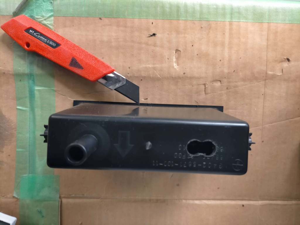 E25キャラバン/いすゞコモの1DINポケット裏面にΦ10mmで開けた2穴をカッターナイフで繋げて長穴に拡大加工した状態。ETC電源線とアンテナ線を同時に通すための配線穴加工工程②