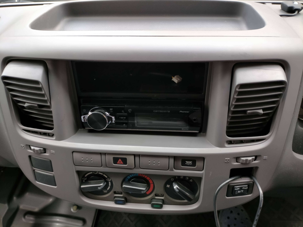 E25キャラバン/いすゞコモのセンタークラスター取り外し手順①・エアコン送風口のルーバーを下向きに向けた状態。送風口の隙間に指を掛けてパネルを引き抜くための準備。工具不要でパネル脱着できる