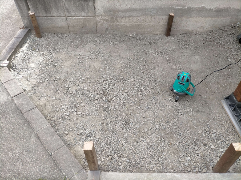 ポーラスコンクリート打設前にレーザー墨出し器（グリーン5ライン）を使って地面の水平を確認しながら均している様子。水勾配不要のポーラスコンクリートでも水平出しで仕上がりがプロ級になる