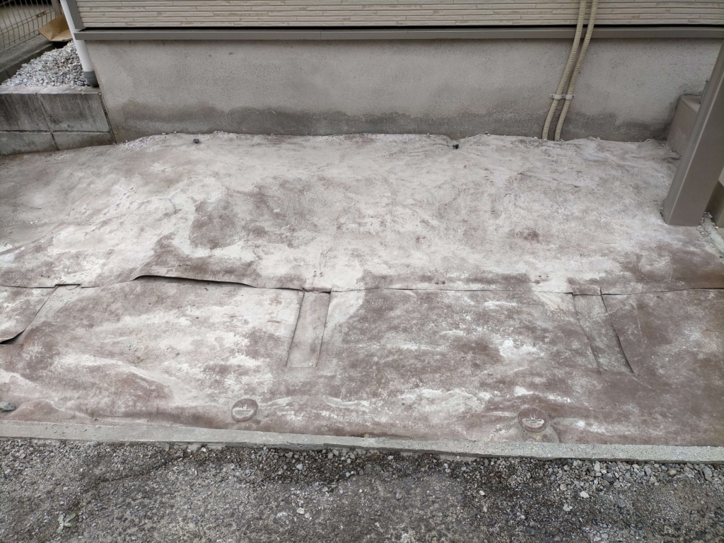 犬走りに敷いていた石灰砕石800kgを土間打ち工事のために撤去した後の防草シートザバーン240の2.5年間の経年劣化を確認する様子