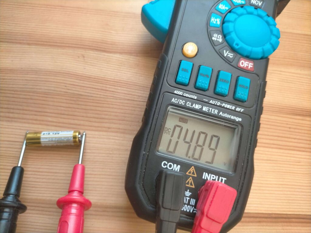 中華FFヒーターのリモコンが効かなくなった27A 12Vアルカリ電池をテスターで電圧測定した結果。5年使用後の電圧降下を確認する写真。テスターによる電圧確認でリモコン不具合の原因が電池切れか本体・ペアリング不良かを切り分けるトラブルシューティング