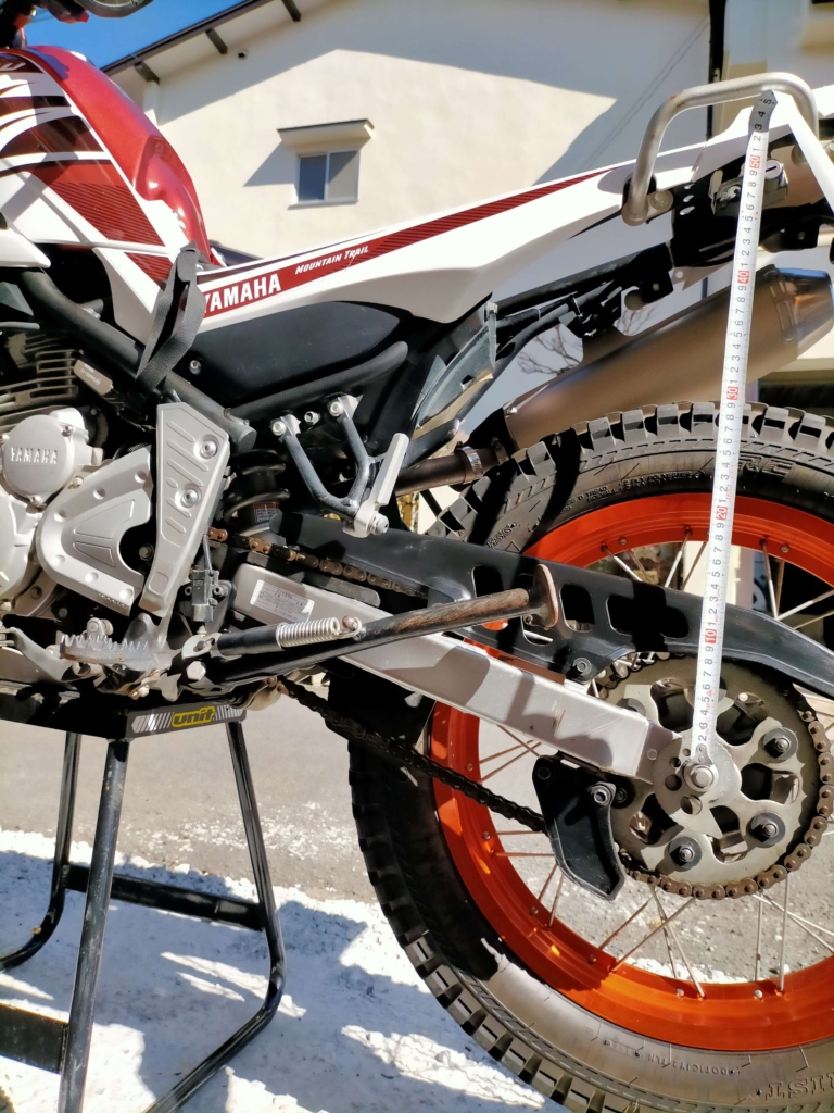 セロー250をメンテナンススタンドに載せてリアサスペンションのサグ出しを行う0G状態でアクスルナット～ヘルメットホルダー鍵穴間を490mmと計測した状態（1G乗車時目標60mm差＝430mm）